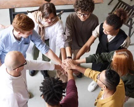 A diverse group of professionals joins hands in a team-building exercise indoors.