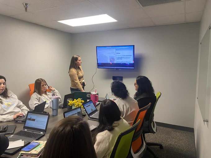 Group of digital leaders at a conference table with one member presenting on a tv.