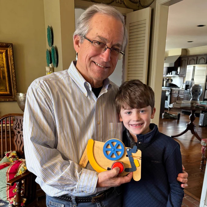 Image shows two individuals, a grandfather and a grandson, smiling and holding a CrunchLabs Disc Launcher in a home's living room.
