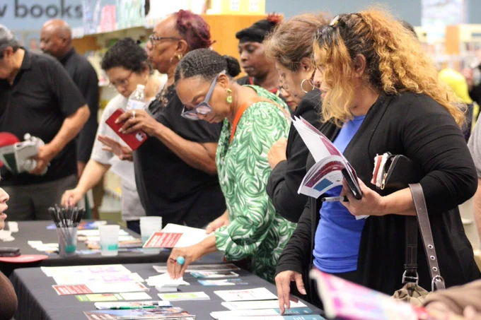 A group of people browsing through flyers on a table.