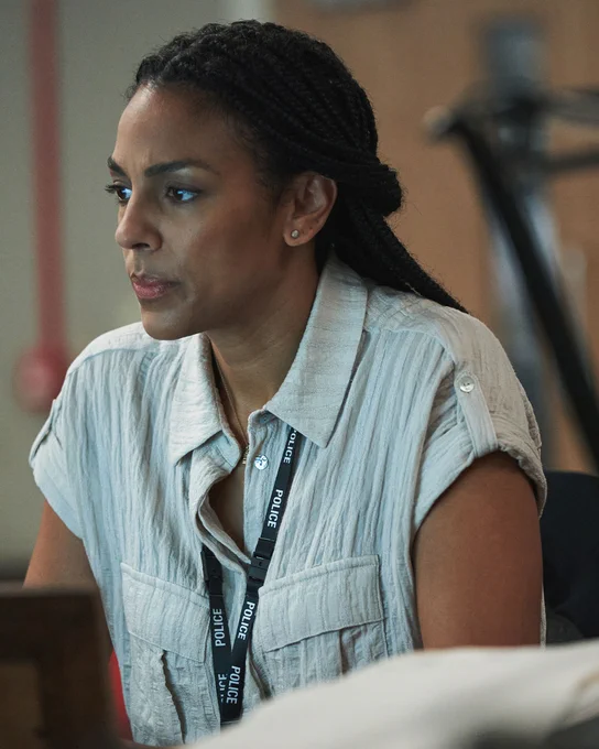A detective in a white shirt with a lanyard around her neck looks at her computer screen with a worried look on her face. 