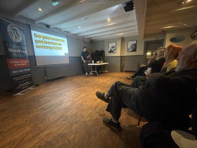 Banner, projector screen showing slide, presenter and front row audience