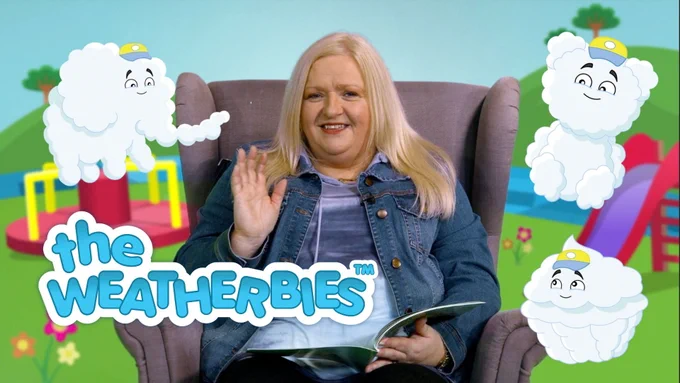 A woman with blonde hair smiles and waves in an armchair, against a backdrop of an animation of a children's playground, with Colin Cloud arranging himself into different shapes around her. He's forming an elephant, a teddy bear, and a cupcake. The Weatherbies logo is in the foreground.
