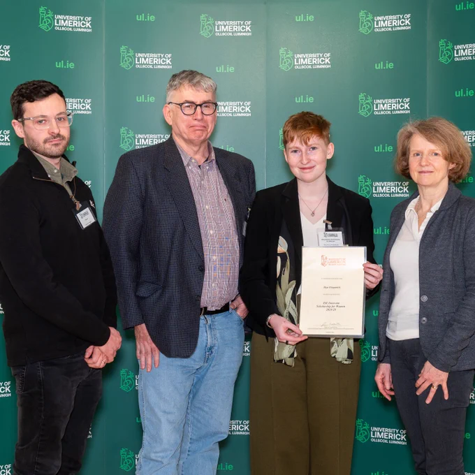 Immersive Software Engineering student Skye Fitzpatrick surrounded by University of Limerick staff holding a certificate to represent that he received the Intercom  Scholarship for Women 2024-25 at the 2025 UL Scholarship Awards Ceremony. There is a green backdrop with ul.ie and the UL logo as a repeating pattern.