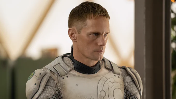 Murderbot (played by Alexander Skarsgård) looks menacingly at someone off screen. It is wearing its suit, with the helmet removed.