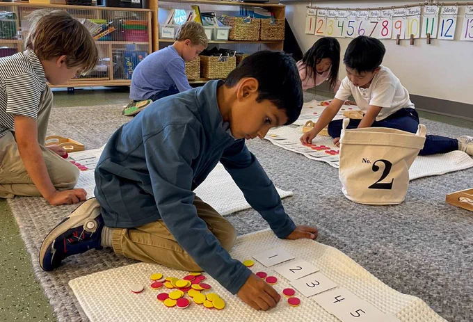A photo of students working on their classroom floor. Each student has a pile of red/yellow chips and they are putting those chips in 10 frames in order to count them.