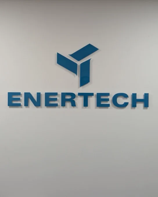Blue acrylic 'Enertech' logo sign installed on white painted wall.