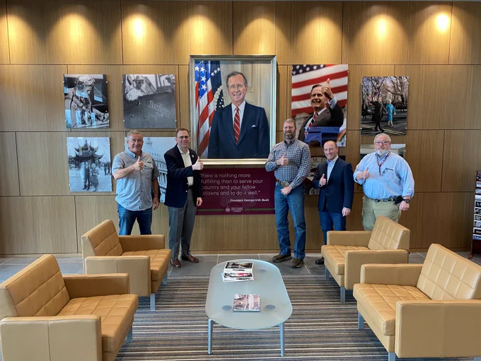 Five men standing in front of the George H.W. Bush tribute wall.
