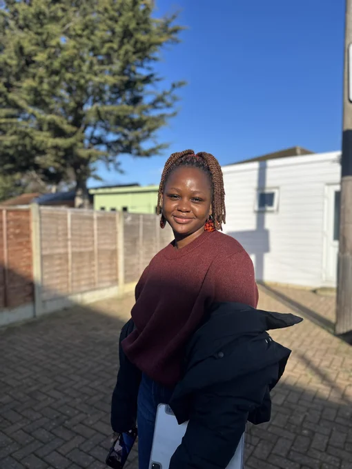 Liz wearing a wine/burgundy sweater, with clear blue skies, a green tree, and a white building behind her. She’s holding her phone and her iPad.