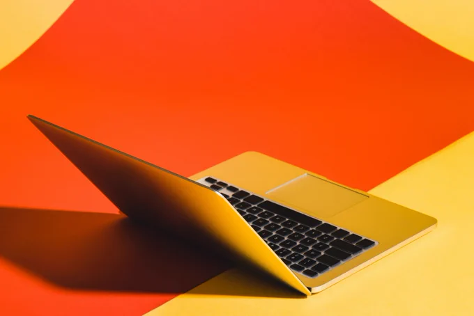 An open laptop on a surface with red and orange diagonal backgrounds.