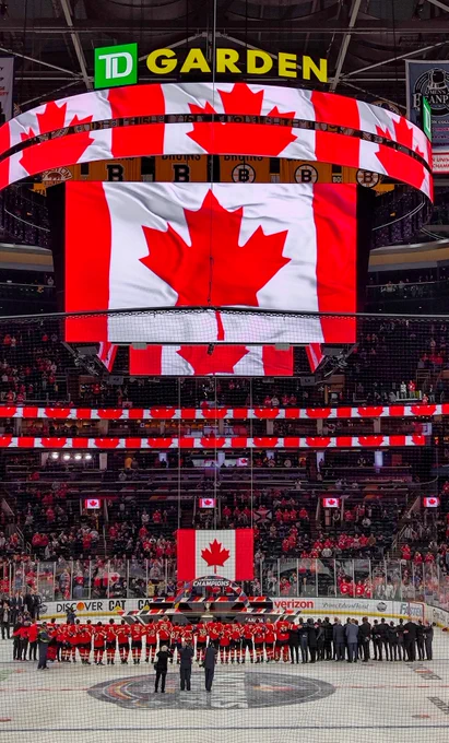 The entire Canadian team standing on ice for O Canada and looking up at a Canadian flag. Above them is a Canadian flag on the big screen.