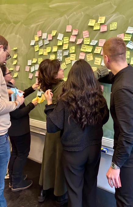 Teilnehmer und Teilnehmerinnen verteilen PostIts an einer Wand