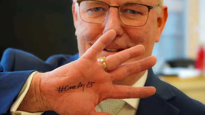 Minister holding his hand up showing #CareDay25 written on his hand