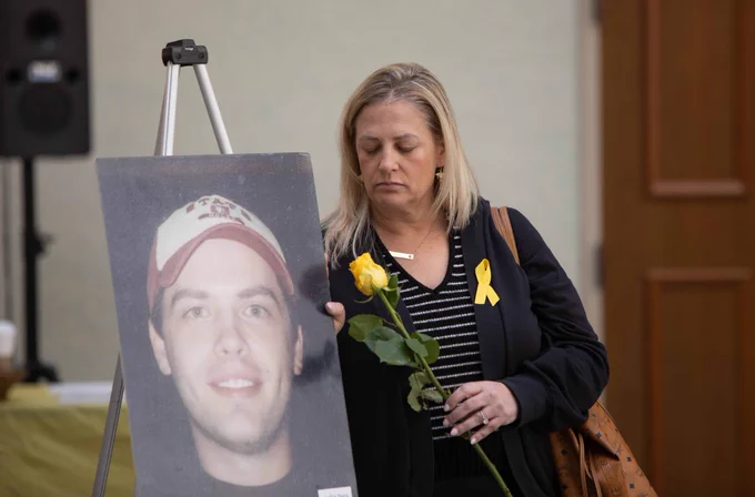 a person holding a yellow rose standing next to a picture
