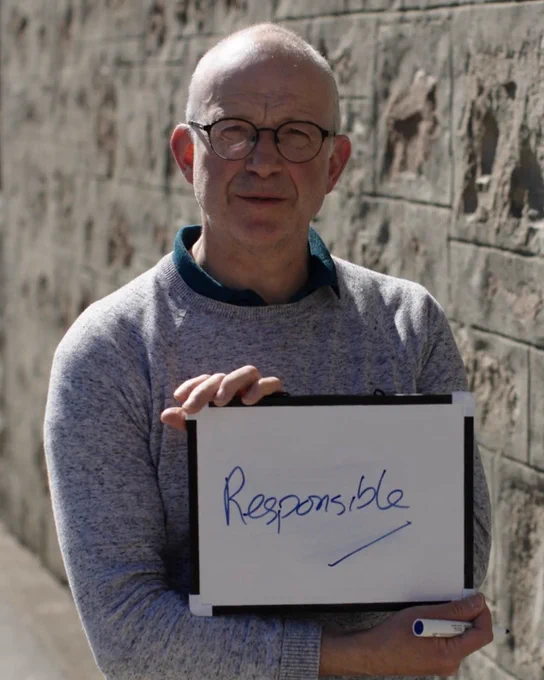A man standing, smiling and holding a board reading "responsible".