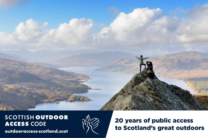 Two people standing at the top of a hill with a loch and more hills in front of them. Text on image: 20 years of public access to Scotland's great outdoors.