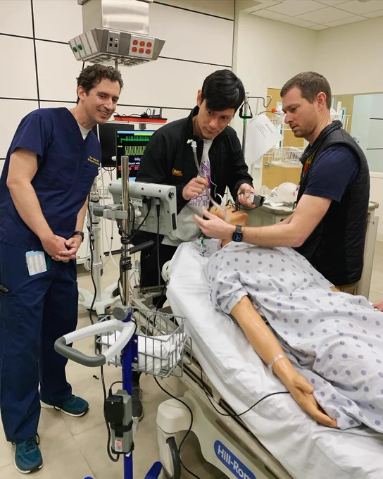 Three doctors work on intubating a simulation manikin.