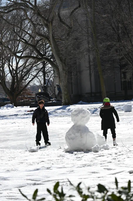 Two students skate outside near a snowman.