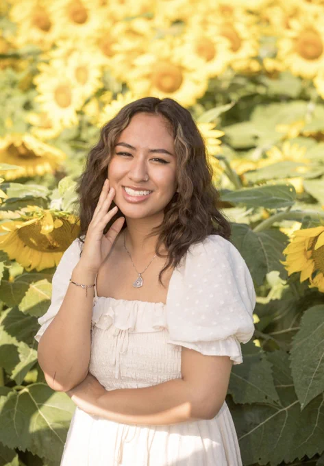 A young woman in a white shirt in front of yellow sunflowers