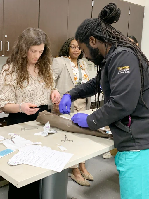 Surgery residents and simulation center visitors suture task-trainer simulated manikin arms.
