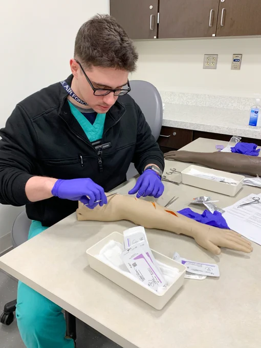 A surgery resident sutures a task-trainer simulated manikin arm.