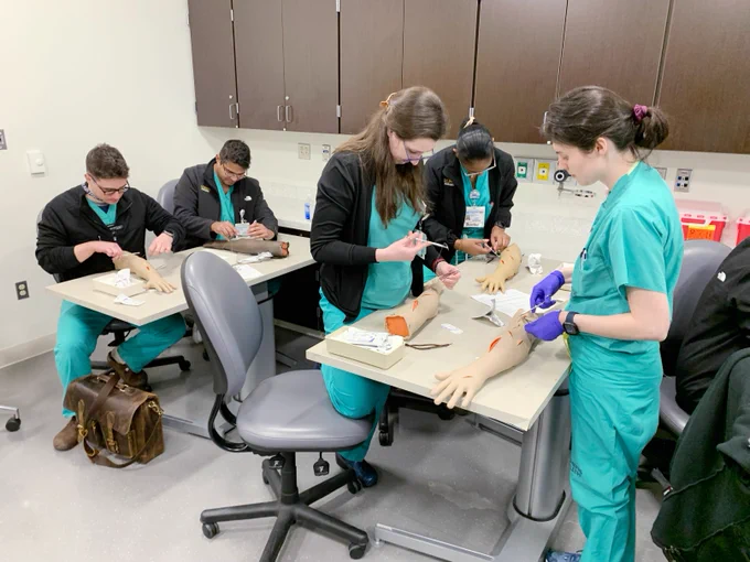Five surgery residents suture task-trainer simulated manikin arms.