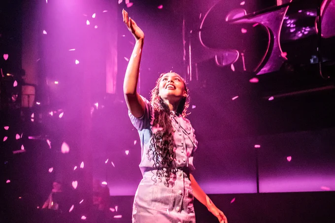 A photo showing a performer embracing petals on a pink-tinged stage 