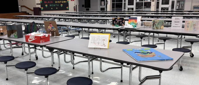 Student artwork displayed on tables in a cafeteria