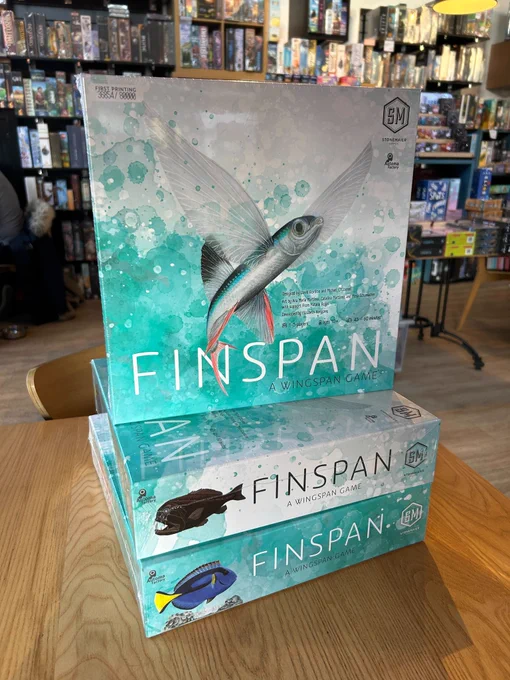 The board game Finspan in the board game shop Ancient Robot Games. The game has an illustration of a fish on a blue background. Boxes of board games can be seen on the background of the image.