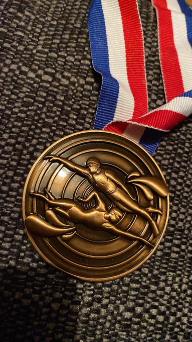 A bronze medal on a white blue and red ribbon. The medal has two swimmers swimming across it