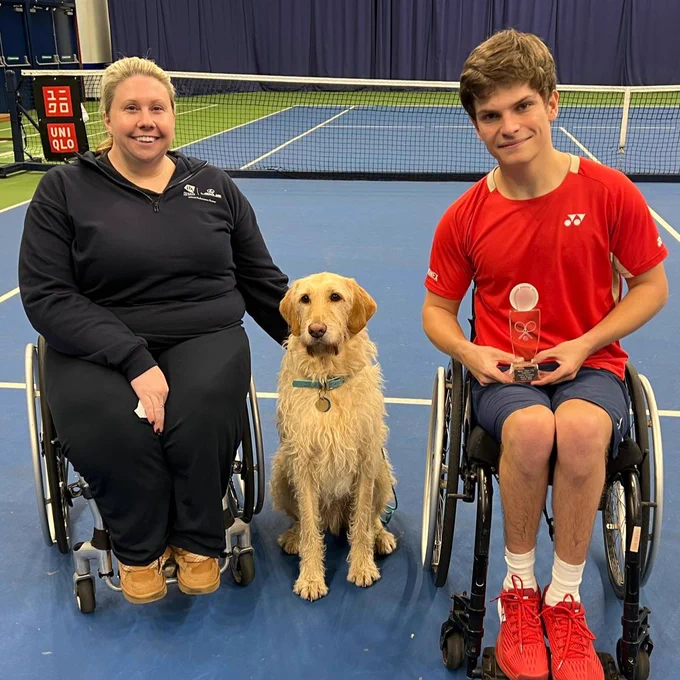 British wheelchair tennis player Greg Slade with his trophy for winning the Bolton Indoor ITF 2 quad singles title at Bolton Arena. Greg is pictured alongside his sister's assistance dog and tournament director Louise Hunt Skelley