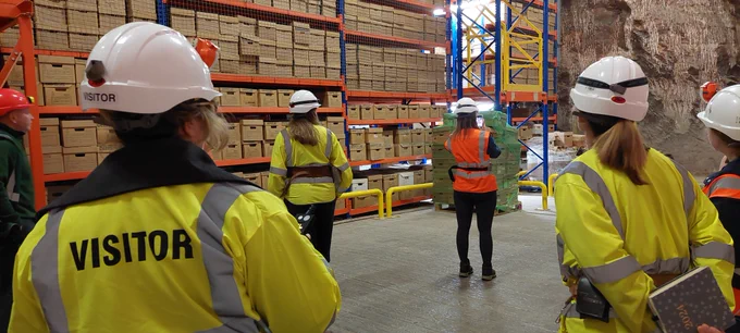 Photograph of Rylands staff in PPE stood in front of a tall shelving unit filled with brown archive boxes. 