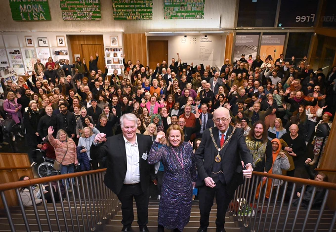 The Director of the Gallery with Walsall Council's Chief Exec and the Mayor of Walsall stand cheering in front of a crowd of visitors, friends and staff.