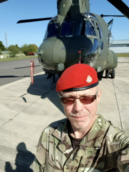 A solider in red beret and army camouflage stands in front of a helicopter