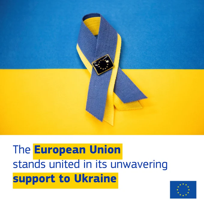 A ribbon in the colours of the Ukrainian flag (blue and yellow) is pinned with a badge featuring the European Union flag. The background also displays blue and yellow colours. Below the image, a message reads: "The European Union stands united in its unwavering support to Ukraine," with "European Union" and "support to Ukraine" highlighted in bold blue text on a yellow background. The European Union flag appears in the bottom right corner. 