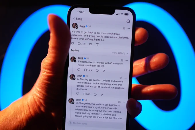A stock photo showing a hand holding up a phone in front of Meta's logo with messages from "Zuck" on screen.