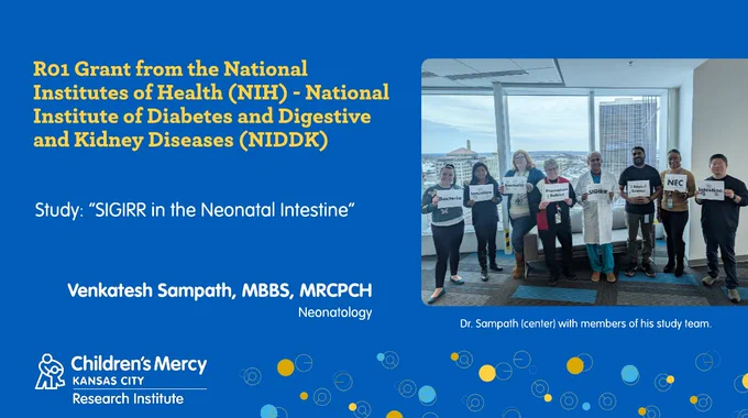 This graphic has a medium blue background. On the right is a group photo of Dr. Sampath standing in the middle with members of his lab and study team standing on either side of him. Each person is holding a white piece of paper with words such as "Bacteria", " Premature Babies", and "SIGIRR" printed on it. On the left is text that explains who Dr. Venkatesh Sampath, MBBS, MRCPCH, Neonatology, received funding from: "R01 Grant from the National Institutes of Health (NIH) – National Institute of Diabetes and Digestive and Kidney Diseases (NIDDK)". Study: "SIGIRR in the Neonatal Intestine"