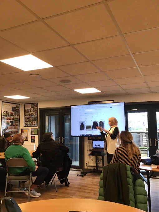 A lady talking about online shopping in a classroom setting with a screen showing some coats for sale.