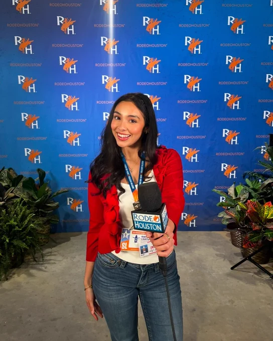 Person holding a microphone with a RodeoHouston tag, standing in front of a backdrop with multiple RodeoHouston logos.