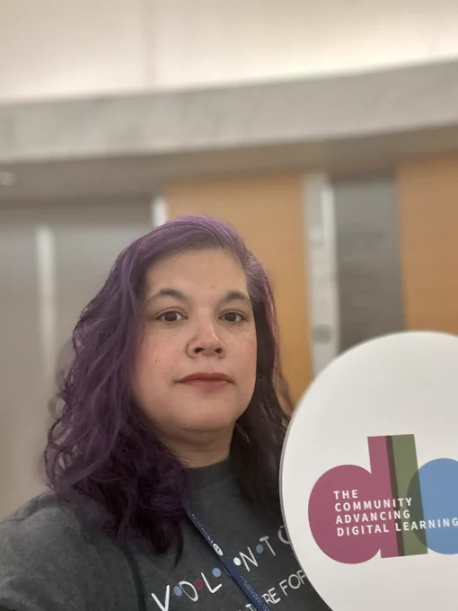 Wendy wearing a voluntold shirt holding a dlac sign that says the community advancing digital learning