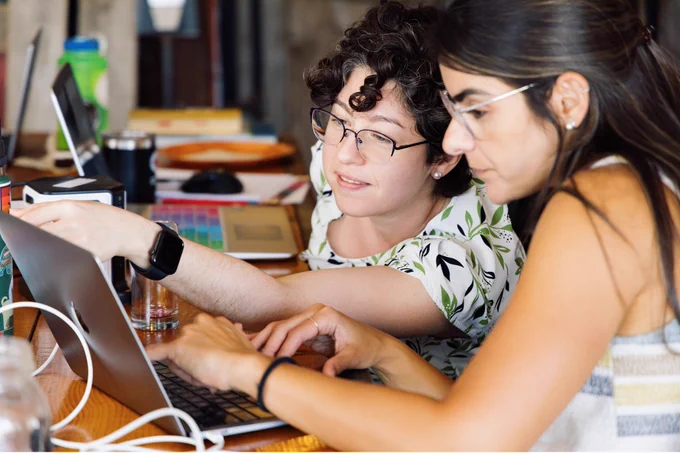 One woman helps another with her writing on a computer.