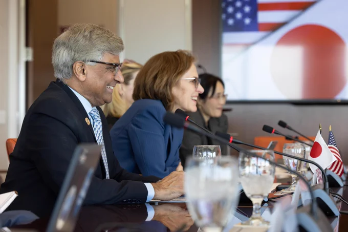 A group of individuals in business formal attire have a discussion at a conference table.