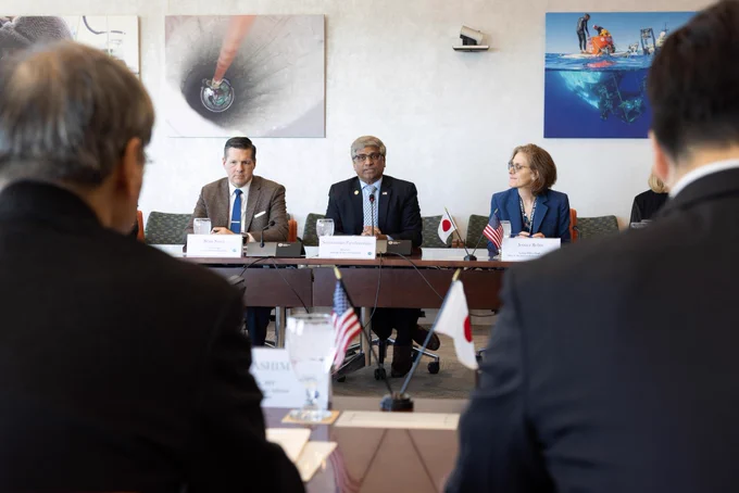 A group of individuals in business formal attire have a discussion at a conference table.