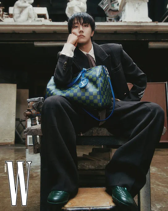 W Korea Cover Image of j-hope sitting, wearing a suit with a LV checkered bag on his right leg, with right arm bent and resting with his hand under his right cheek. Logo-embellished cropped jacket and pants, shirt, tie, LV footprint soccer sneakers, chain belt and Speedy bag are all by Louis Vuitton.
