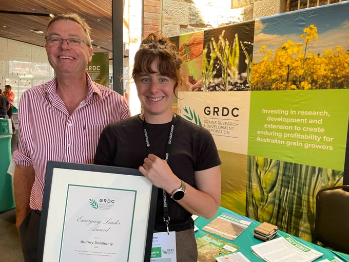 Cam Nicholson (left) and Audrey Delahunty (right posing at a GRDC exhibition stand,. Background banners highlight agricultural landscapes and the GRDC logo, emphasising investment in grain research and development.