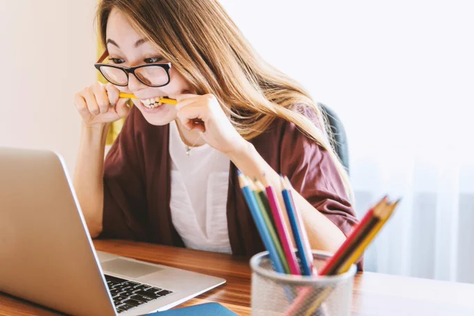 a photograph of a woman looking excitedly at a laptop while biting a pencil