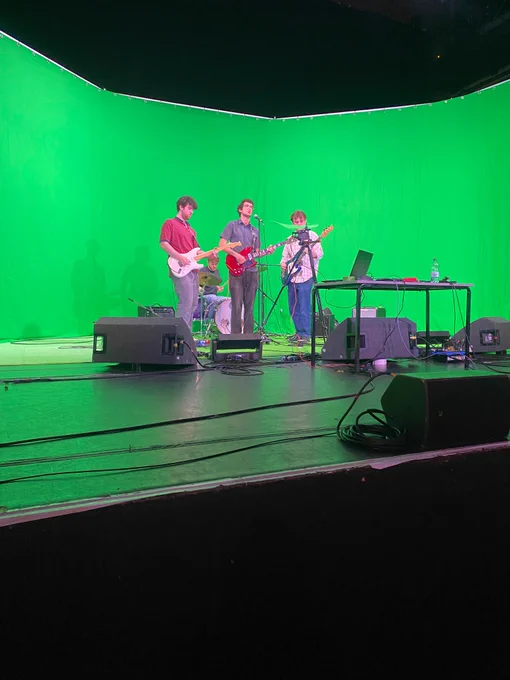 The band on stage at the Corn Exchange in front of a green screen