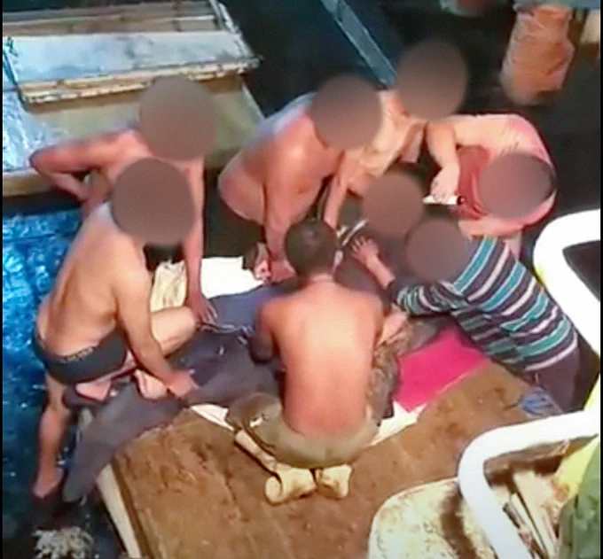 Group of people with their faces blurred, all on top of a marine animal that has been killed