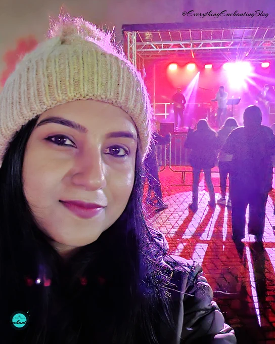  image includes a selfie of UK travel blogger Anamika A Chattopadhyaya in the foreground with the Tom Betts band performing on stage in the background under vibrant red and purple lights at cinch stadium Franklin's Gardens, Northampton, captured for everything enchanting blog.