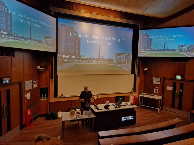 Peter at the front of a lecture theatre holding some cake props